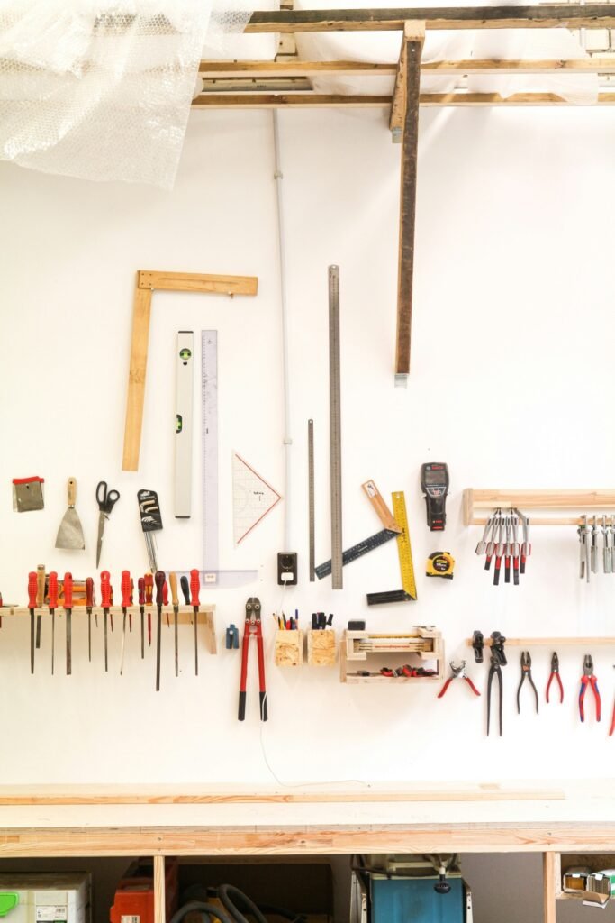 Organized workshop wall with neatly arranged hand tools, rulers, clamps, and measuring instruments above a wooden workbench.