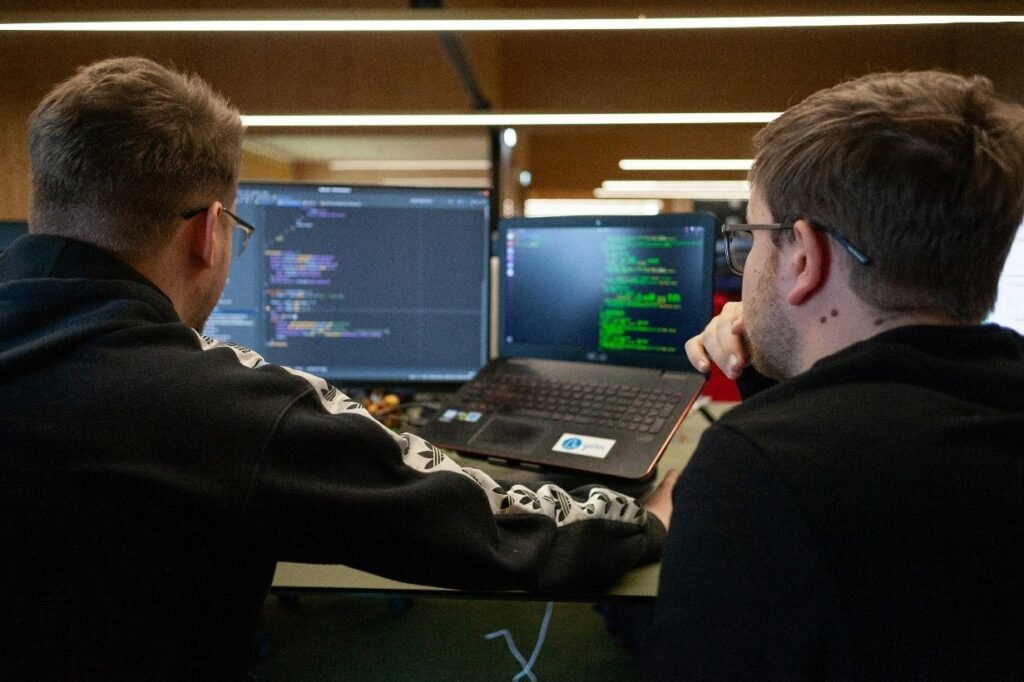 Two software developers working at laptops with code displayed on screens in a modern office environment