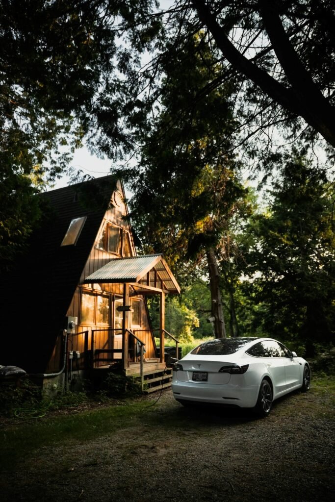 Tesla electric car parked outside a modern cabin home surrounded by trees, showcasing smart living